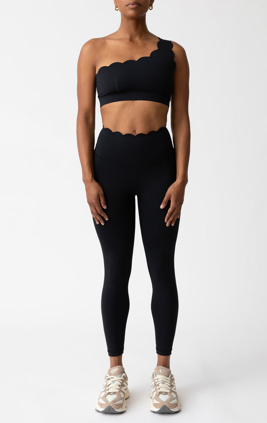 Person wearing a black scalloped sports bra and leggings set on a white background